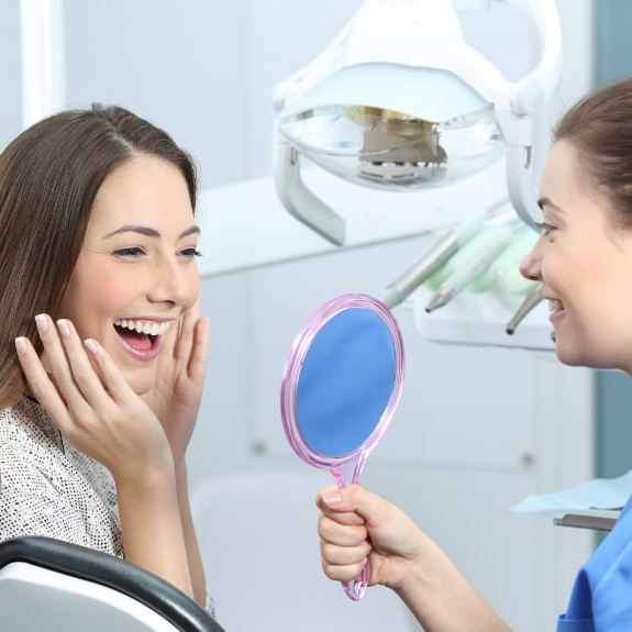 Dental patient beaming at her new smile in a mirror