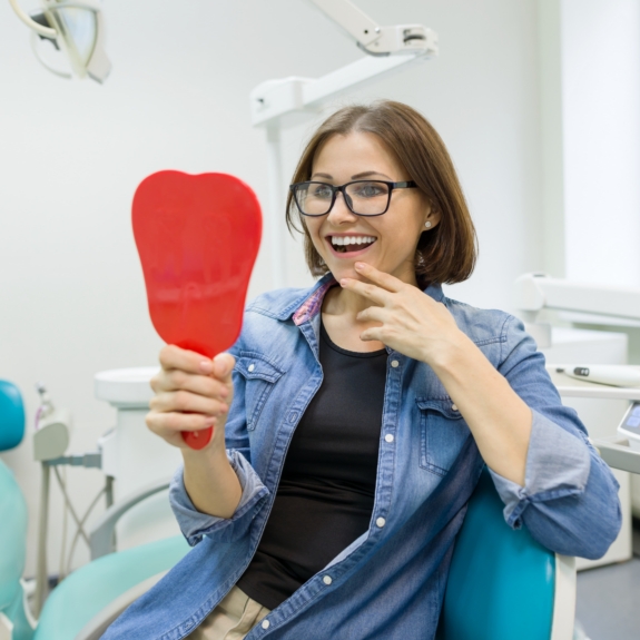 Young woman in the dental chair looking at her smile in a mirror