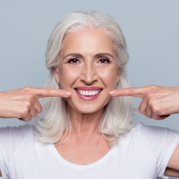 Woman with long gray hair pointing to her smile
