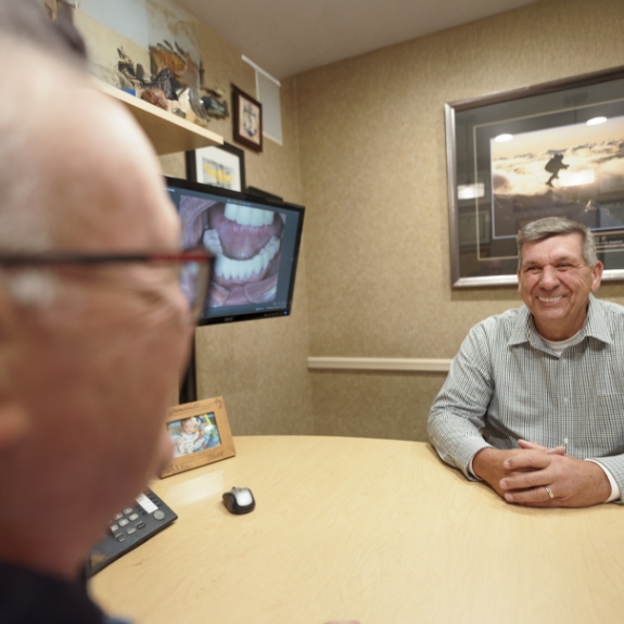Man sitting across a desk from his Massapequa Park cosmetic dentist during a consultation