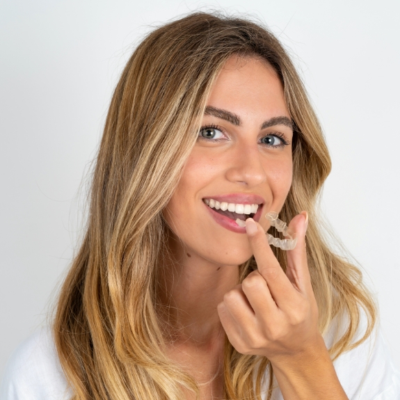 Smiling blonde woman holding an Invisalign aligner near her mouth