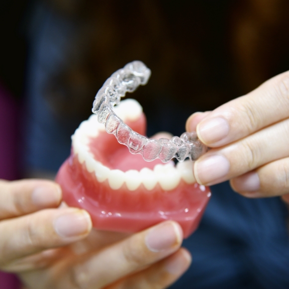 Dentist plcing an Invisalign aligner over a model of a row of teeth