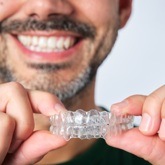 Smiling man holding two Invisalign clear aligners