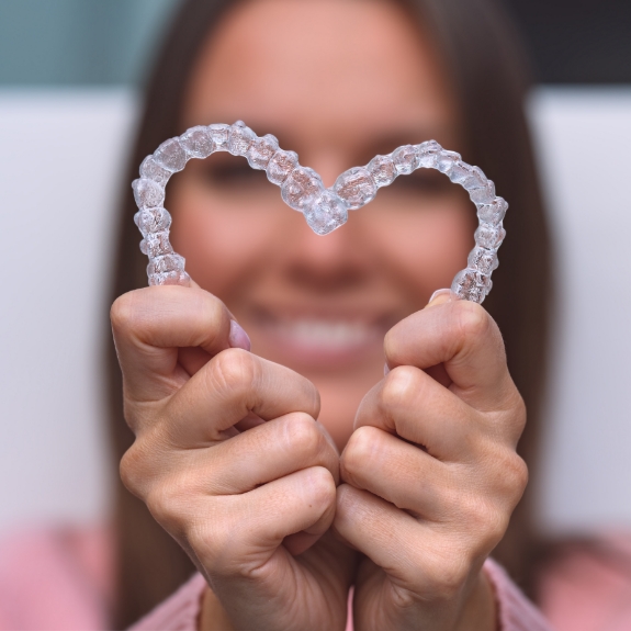 Woman making a heart shape with two Invisalign aligners